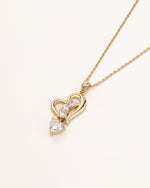 Dancing Heart Necklace in solid gold with moissanite on a soft neutral background.