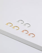 Star Arc Huggie Hoop Earrings in silver, gold, and rose gold colors arranged together, featuring polished stars and open curved hoops.
