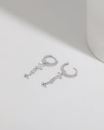Starlight Drop Huggie Earrings shown as a pair on a white surface, with the hoops open to highlight the clasp and dangling star charm design.
