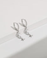 Starlight Drop Huggie Earrings displayed hanging as a pair, featuring pavé hoops, geometric drop stones, and a polished star charm.