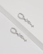 Starlight Drop Huggie Earrings laid flat as a pair on a white surface, showing the slim huggie hoops and delicate star drop details.