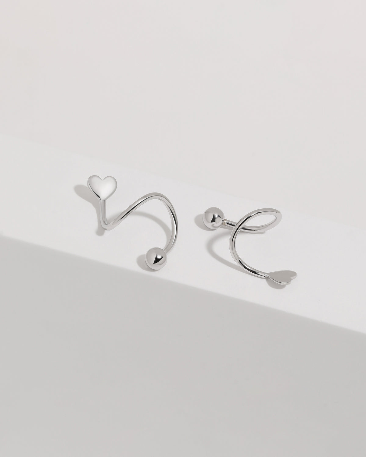 Heart Spiral Screw Back Earrings in 925 sterling silver displayed on a white surface, showing the heart-shaped ends, sculptural spiral curves, and polished ball details.