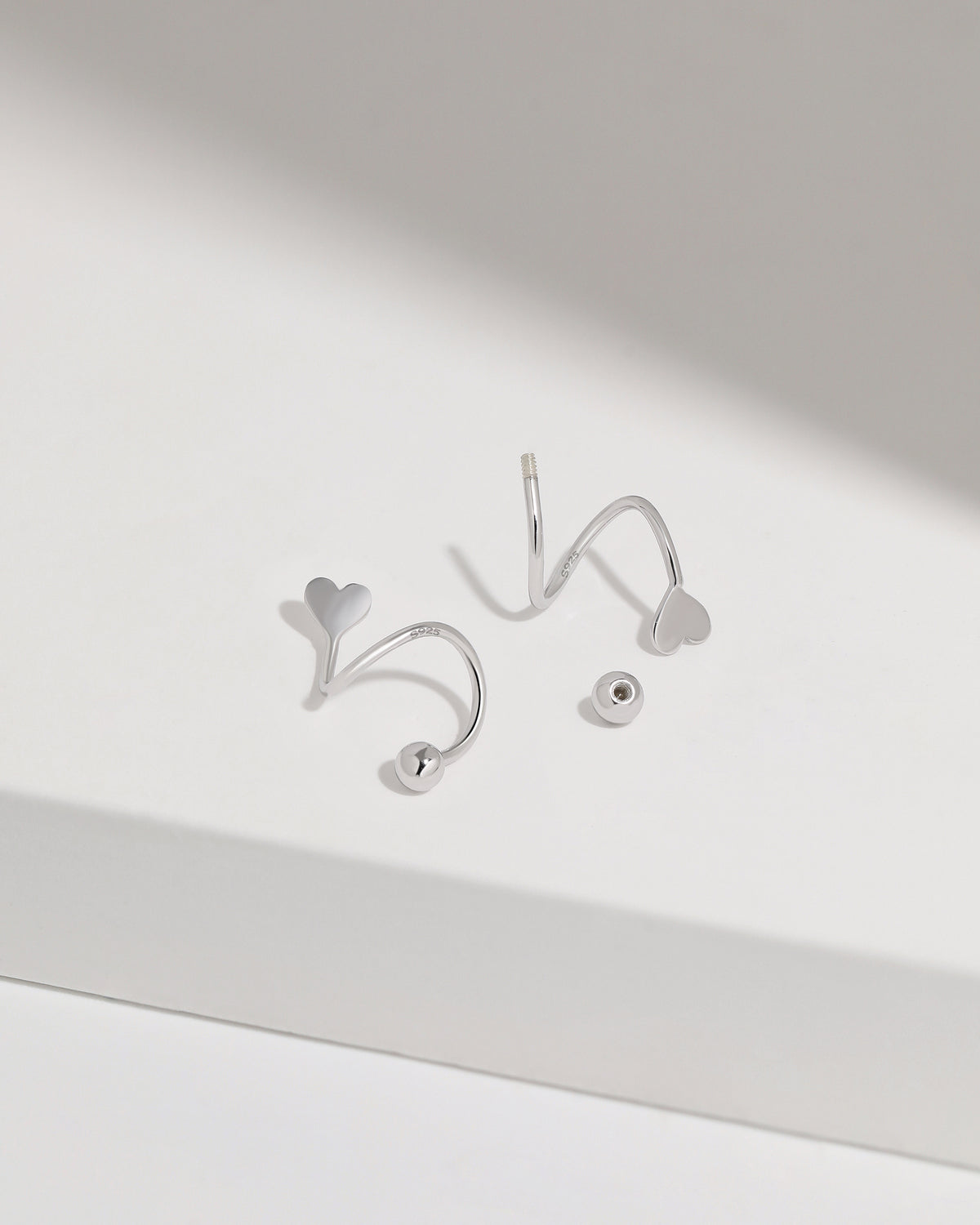 Heart Spiral Screw Back Earrings in silver color displayed on a white surface, highlighting the smooth curved construction, heart-shaped ends, and round screw back balls.
