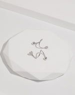 Heart Spiral Screw Back Earrings in silver color displayed on a white geometric surface, showing the sculptural spiral shape, heart ends, and polished round screw back balls.