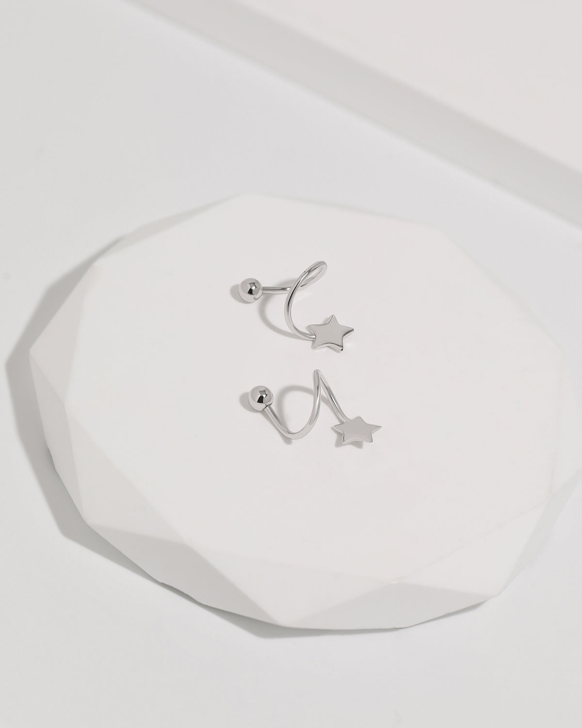 Star Spiral Screw Back Earrings in silver color displayed on a white jewelry platform, featuring star ends, curved spiral posts, and round screw backs.