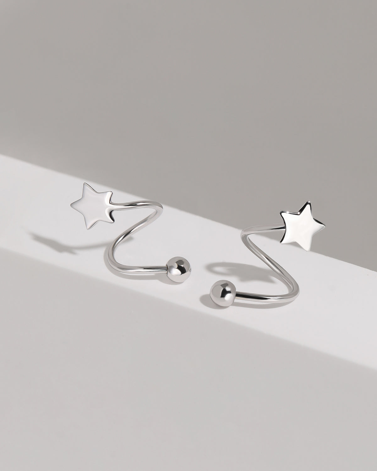 Star Spiral Screw Back Earrings in silver color shown close up on a white platform with polished five-point stars and round screw ball backs.
