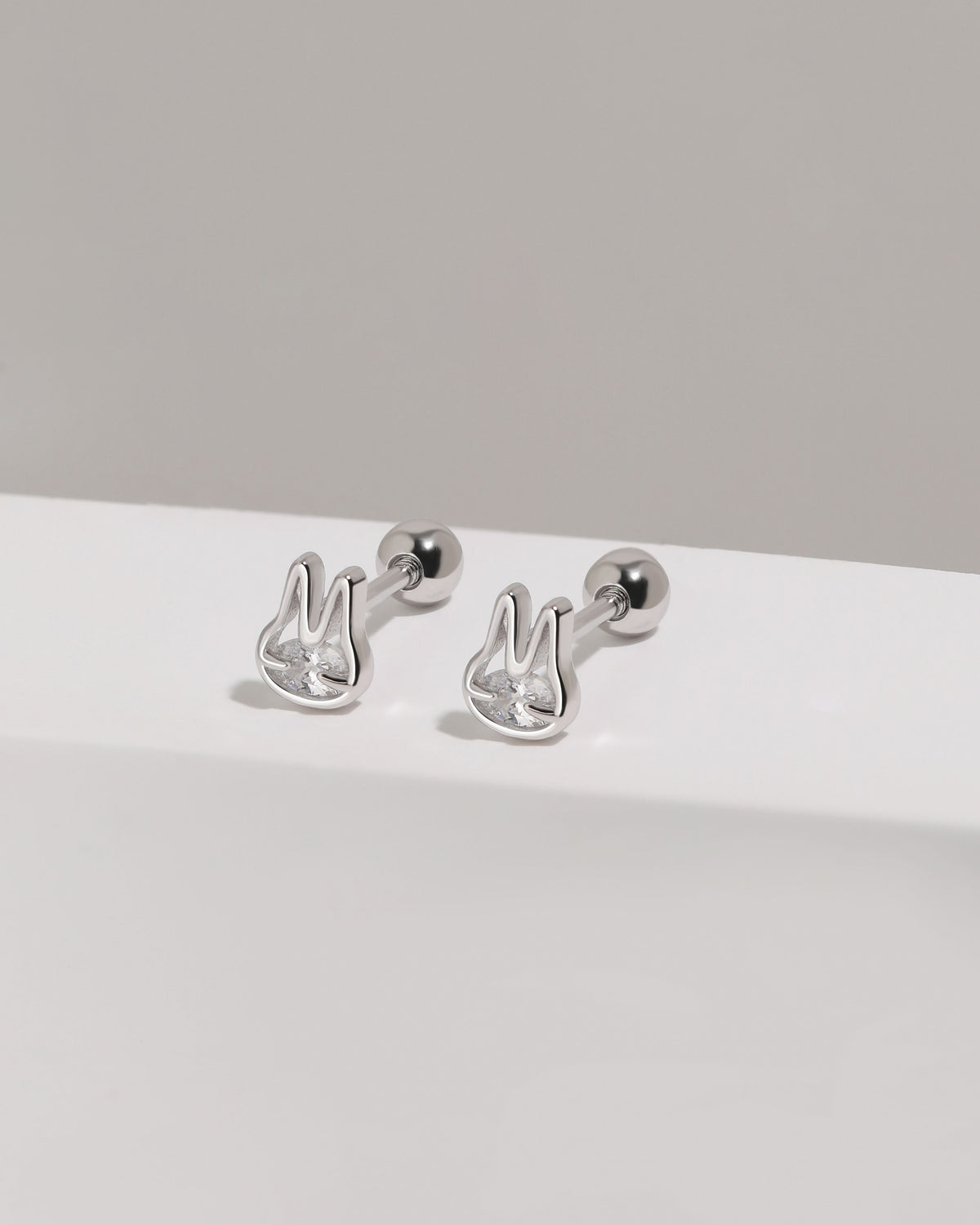Pair of silver Meissa Bunny Sparkle Screw Back Earrings with clear cubic zirconia displayed on a white platform with round screw backs visible.
