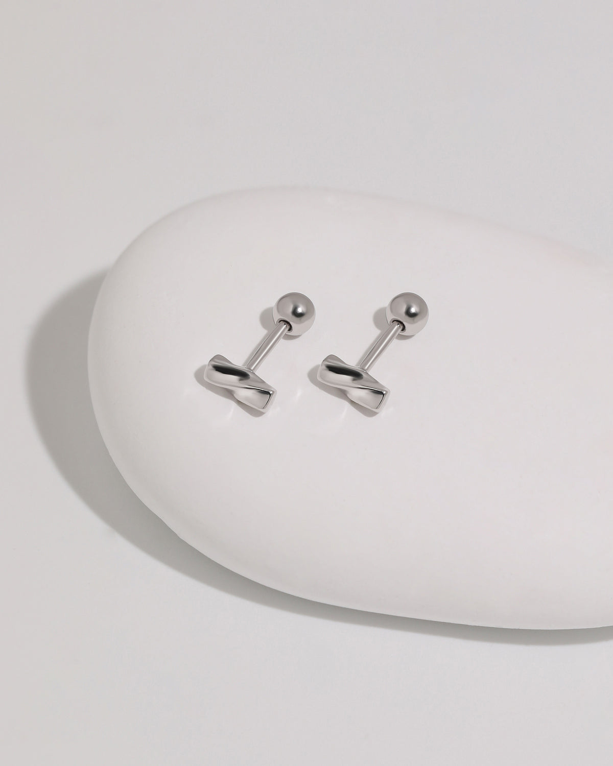 Pair of Twist Bar Screw Back Earrings in polished 925 sterling silver displayed on a smooth white stone with round screw backs visible.