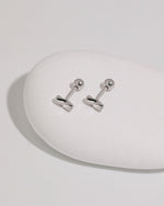 Pair of Twist Bar Screw Back Earrings in polished 925 sterling silver displayed on a smooth white stone with round screw backs visible.