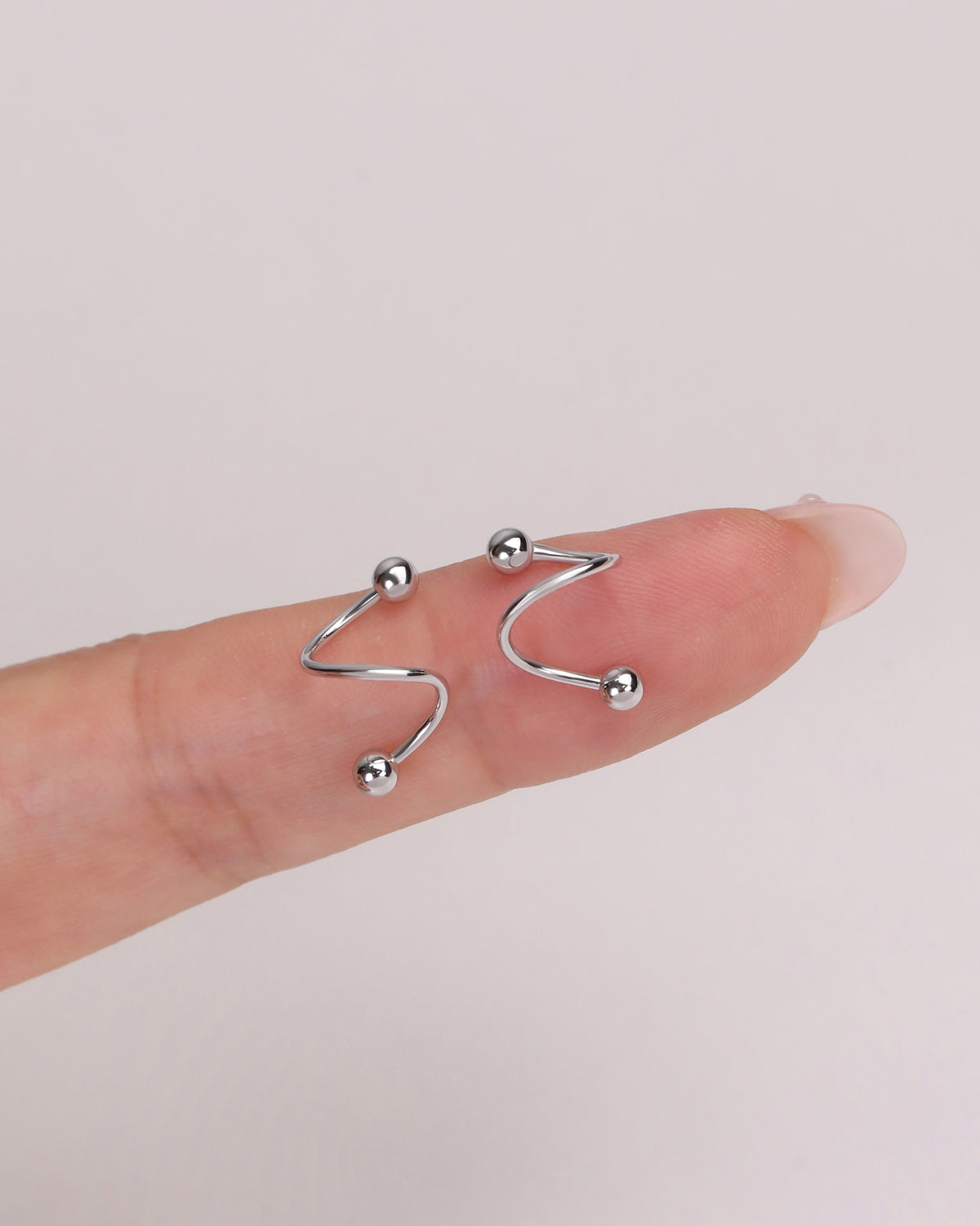 Ball Spiral Screw Back Earrings in silver color displayed on a finger for a close-up view of the curved spiral silhouette and petite size.