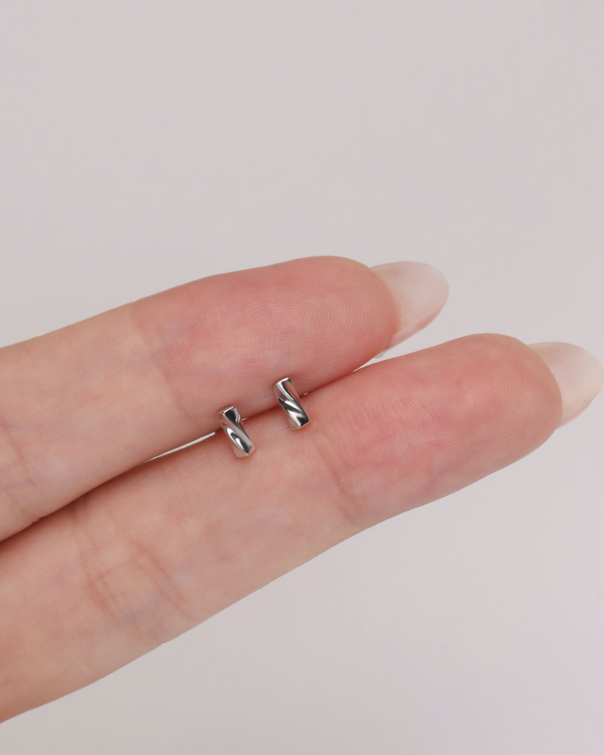 Pair of Twist Bar Screw Back Earrings resting on fingertips, showing the petite polished twist bar design and scale.