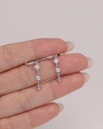 Starlight Drop Huggie Earrings shown on fingertips for size reference, highlighting the petite hoop shape and dangling star charm accents.