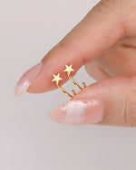 Pair of Star Arc Huggie Hoop Earrings in gold color held between fingers, showing the polished star fronts and curved open hoops.