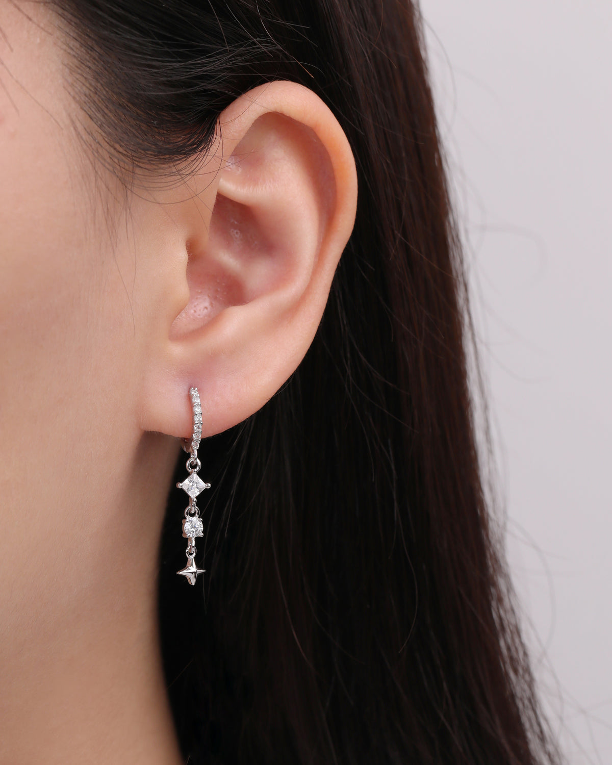 Starlight Drop Huggie Earring worn on the earlobe, showing the slim hoop with sparkling drop stones and a small star charm.