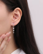 Starlight Drop Huggie Earring worn on the earlobe with a hand near the face, highlighting the elegant drop length and delicate sparkle.