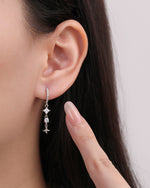 Starlight Drop Huggie Earring worn on the earlobe with a finger pointing beside it, emphasizing the petite size and dangling star detail.