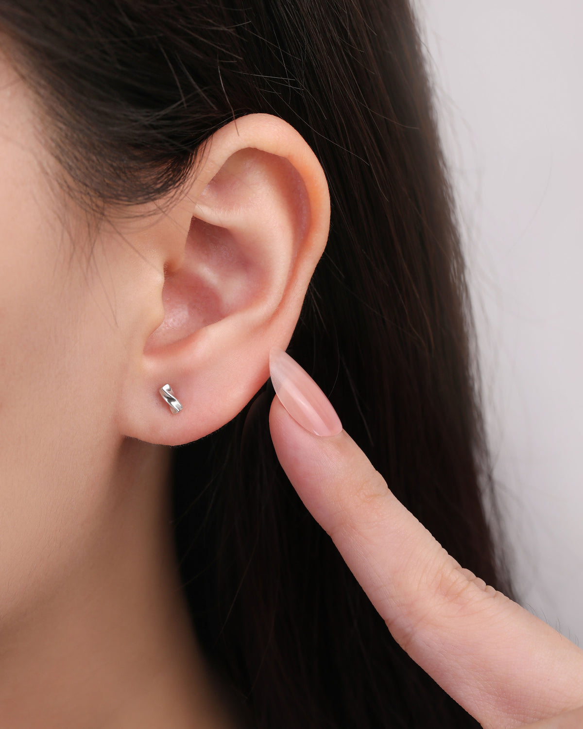 Close-up of a Twist Bar Screw Back Earring worn on the earlobe with a finger beside it to show its petite size and polished finish.