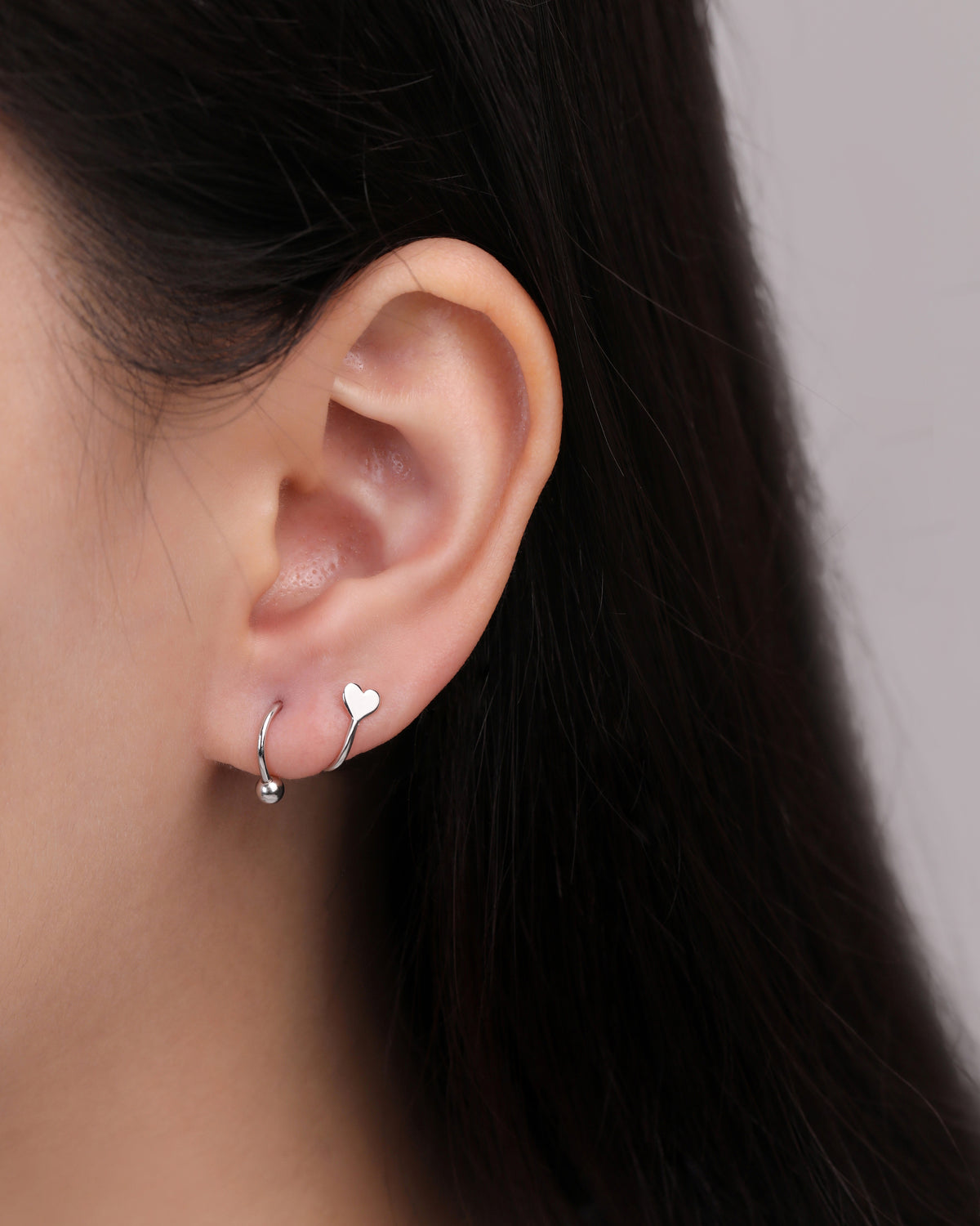 Heart Spiral Screw Back Earring in silver color worn on the earlobe, featuring a delicate heart end, curved spiral design, and polished round ball detail.