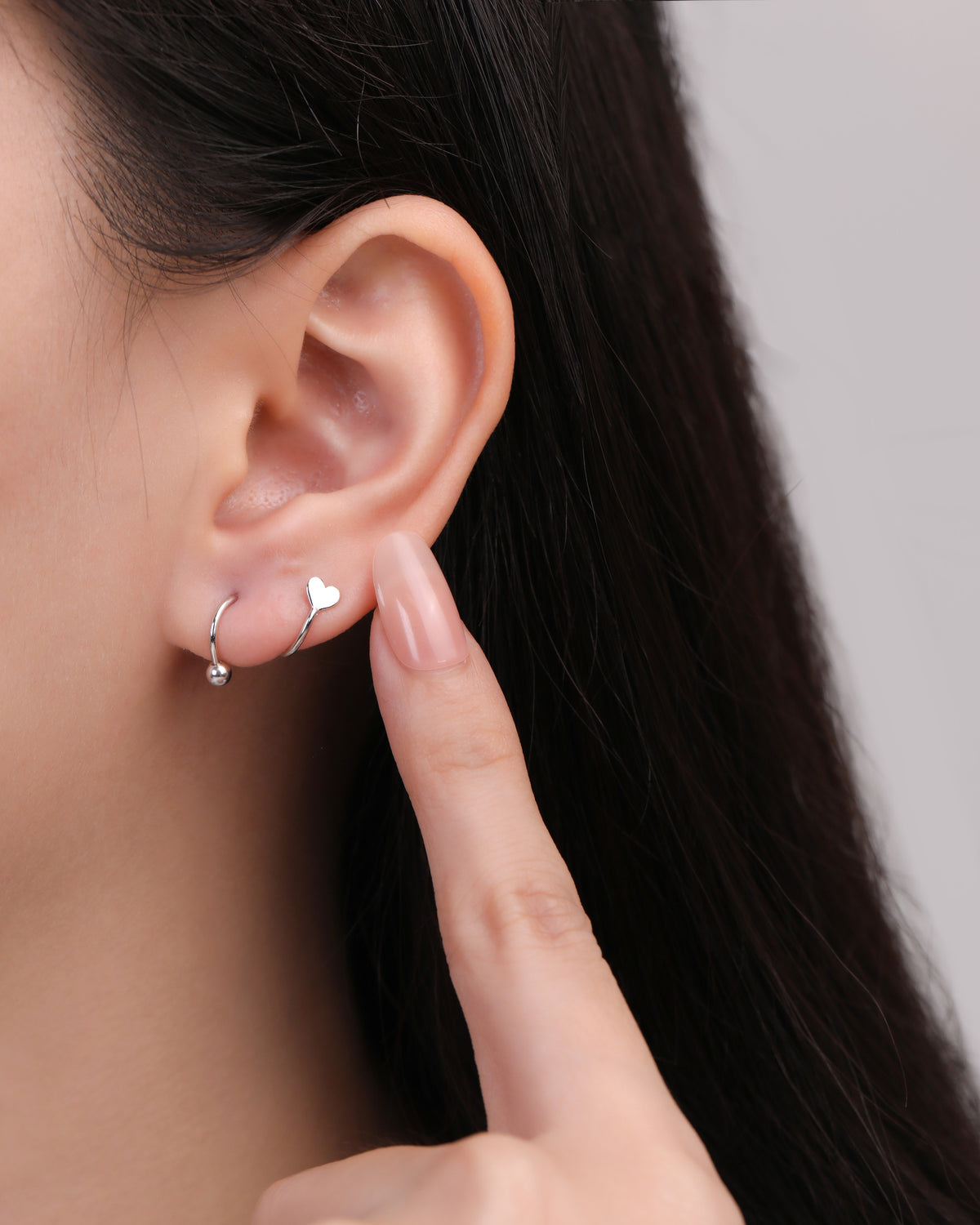 Heart Spiral Screw Back Earring in silver color worn on the earlobe, showing the polished heart detail and curved spiral silhouette with a round ball end.