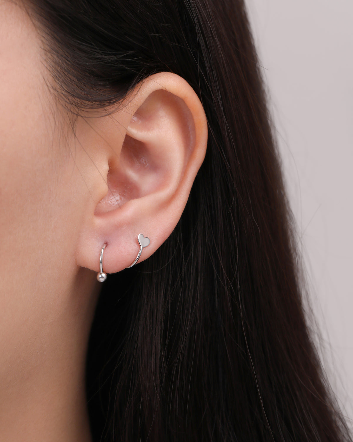 Heart Spiral Screw Back Earring in silver color worn on the earlobe, showing how the curved spiral wraps around the ear with a polished heart and round ball end.