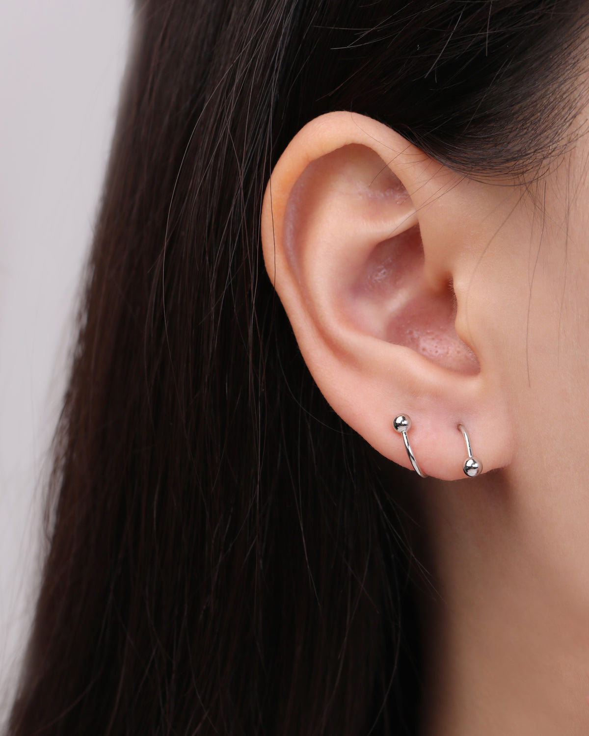 Ball Spiral Screw Back Earring in silver color worn on the opposite ear, showing the mirrored left and right spiral shapes with polished ball ends.