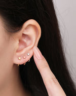 Star Arc Huggie Hoop Earrings in gold, rose gold, and silver colors styled together on the ear to show the three color options.