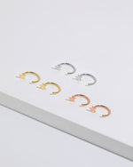 Star Arc Huggie Hoop Earrings in silver, gold, and rose gold colors arranged together, featuring polished stars and open curved hoops.