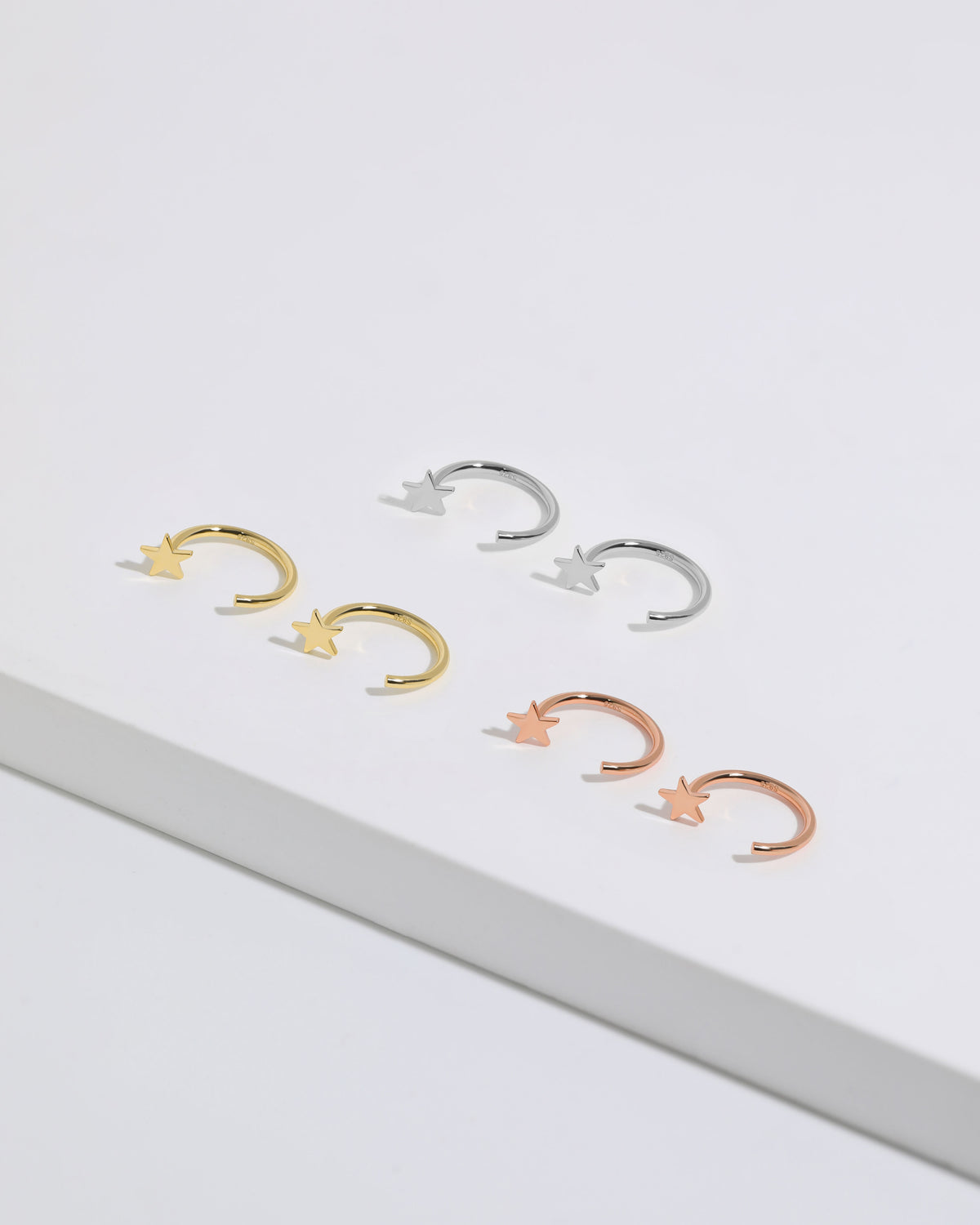 Star Arc Huggie Hoop Earrings in silver, gold, and rose gold colors arranged together, featuring polished stars and open curved hoops.
