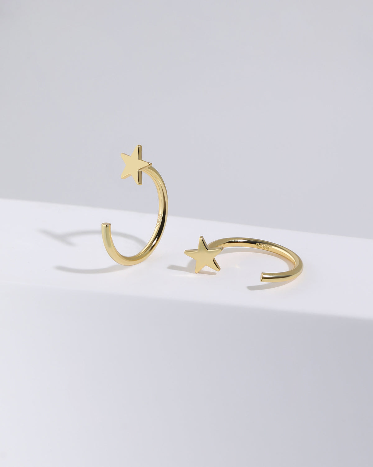Pair of Star Arc Huggie Hoop Earrings in gold color displayed from different angles, showing the five-point star and S925 open hoop design.