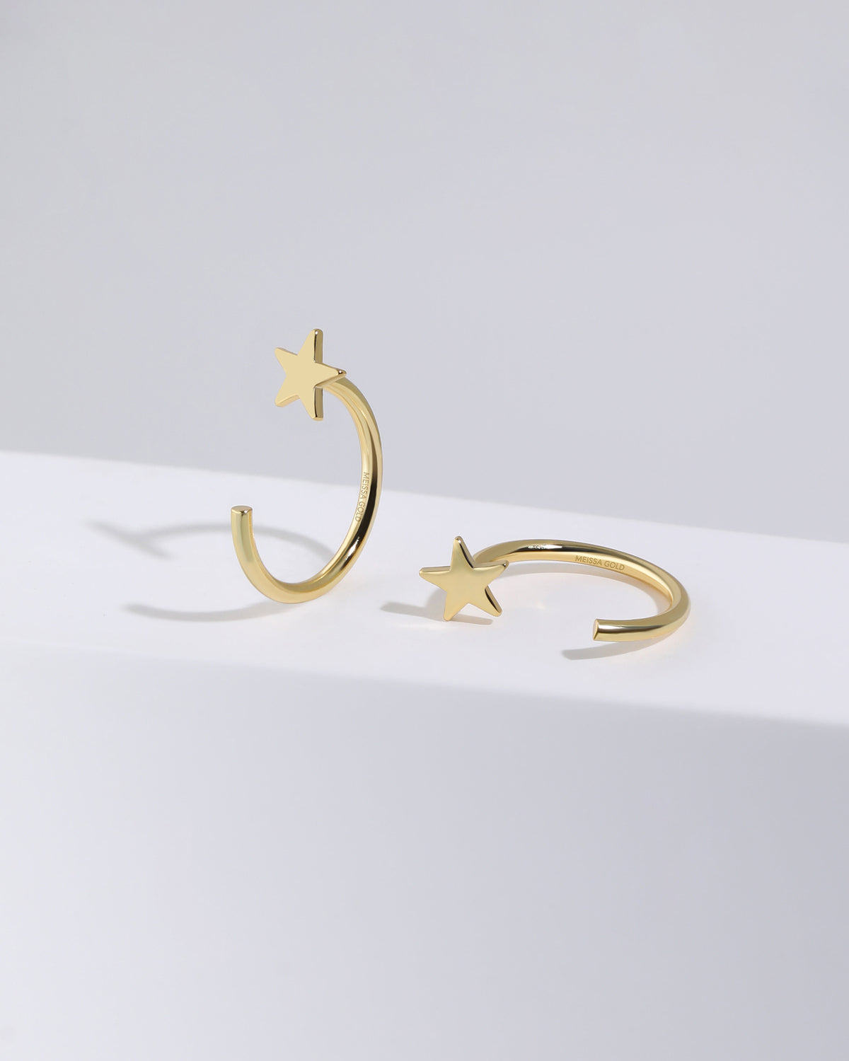 Pair of Star Arc Huggie Hoop Earrings in gold color displayed from different angles, showing the five-point star and open hoop design.