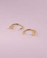 Pair of Star Arc Huggie Hoop Earrings in gold color displayed flat on a pink background with visible S925 markings and polished star details.