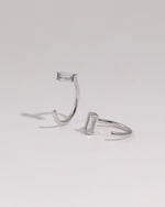 Pair of silver-tone Meissa Baguette Sparkle Huggie Hoop Earrings with clear baguette-cut stones on a neutral background.