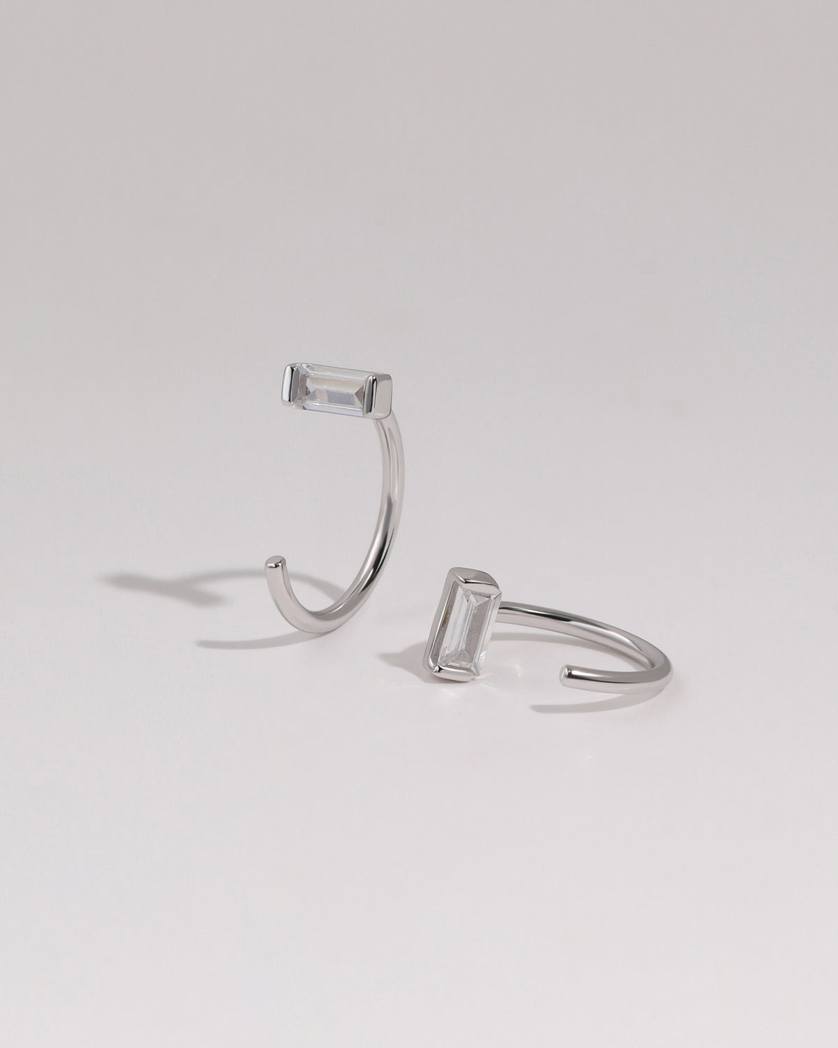 Pair of silver-tone Meissa Baguette Sparkle Huggie Hoop Earrings with clear baguette-cut stones on a neutral background.