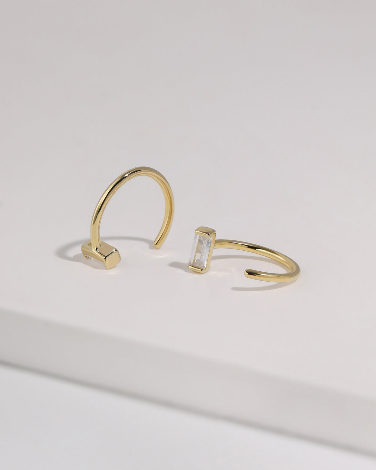 Pair of gold-tone Meissa Baguette Sparkle Huggie Hoop Earrings with clear baguette-cut stones shown from different angles.