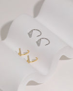 Meissa Sparkling Bar Huggie Hoop Earrings with clear stones in silver-tone and gold-tone colors, displayed on soft white fabric.