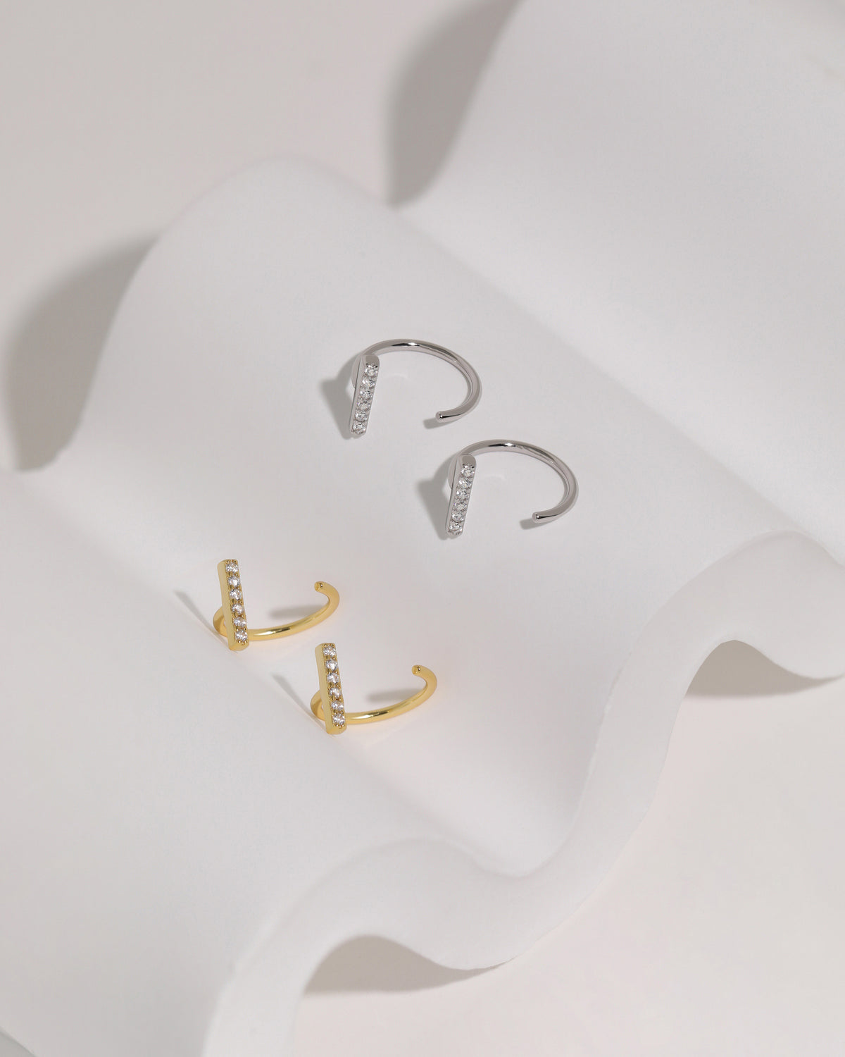 Meissa Sparkling Bar Huggie Hoop Earrings with clear stones in silver-tone and gold-tone colors, displayed on soft white fabric.