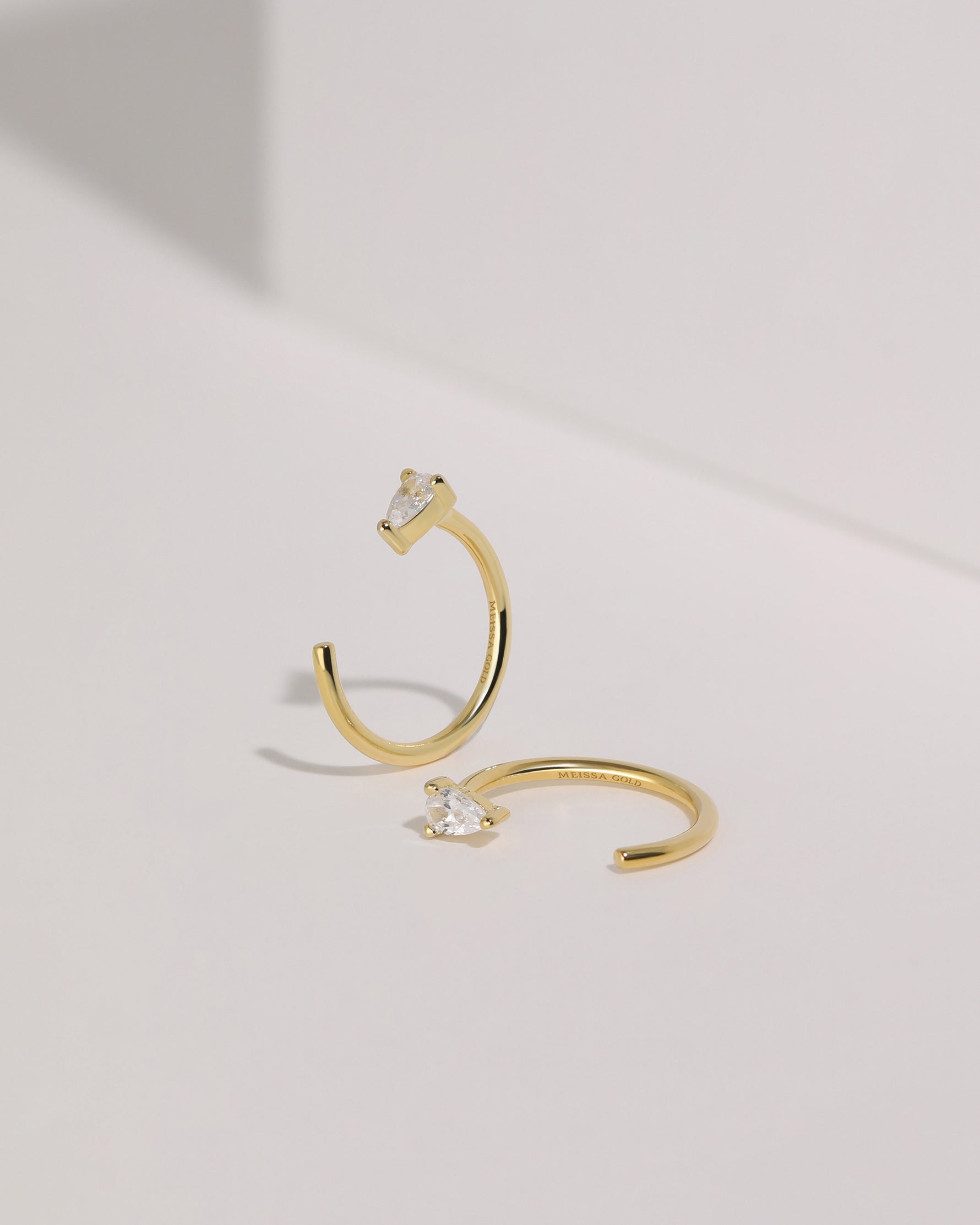 Pair of gold-tone Meissa Pear Sparkle Huggie Hoop Earrings with moissanite displayed on a white surface.