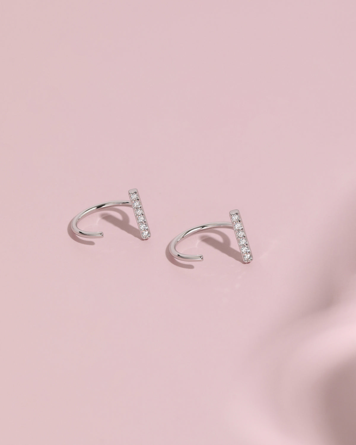 Pair of silver-tone Meissa Sparkling Bar Huggie Hoop Earrings with clear stones on a soft pink background.