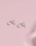 Pair of silver-tone Meissa Sparkling Bar Huggie Hoop Earrings with clear stones on a soft pink background.