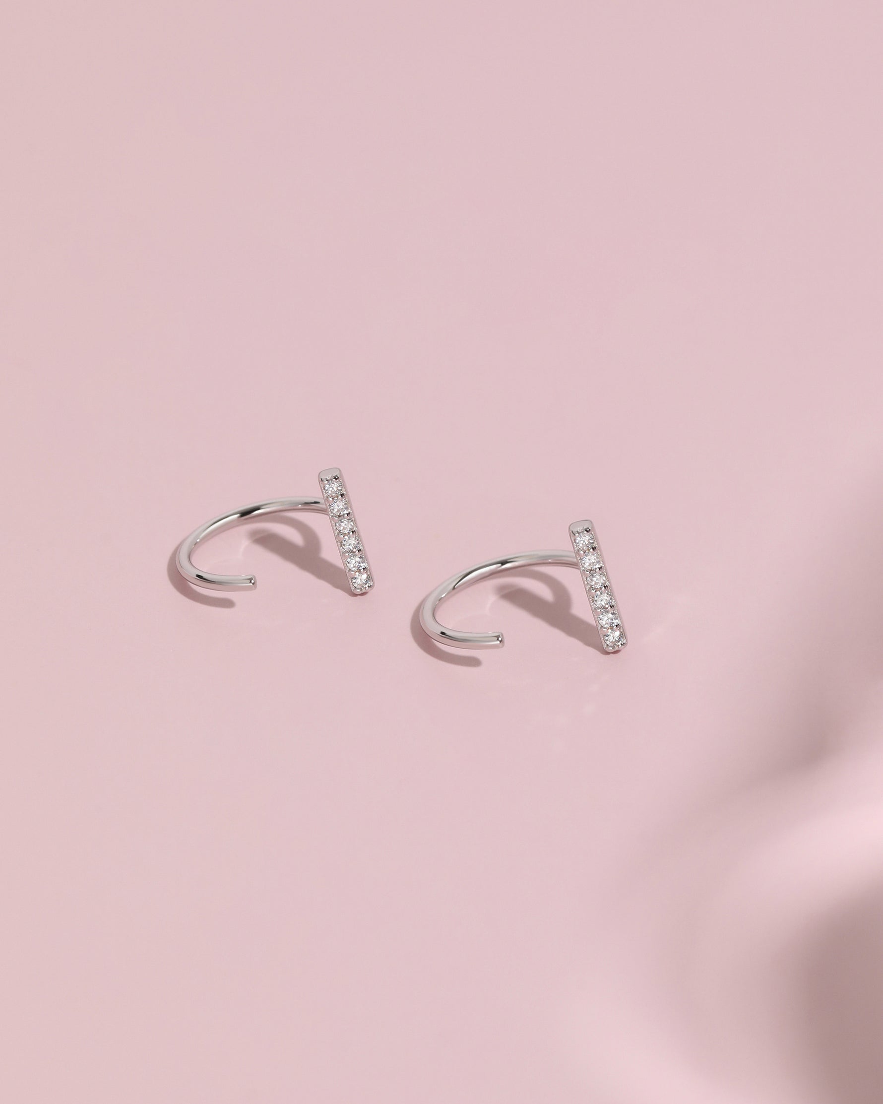Pair of silver-tone Meissa Sparkling Bar Huggie Hoop Earrings with clear stones on a soft pink background.