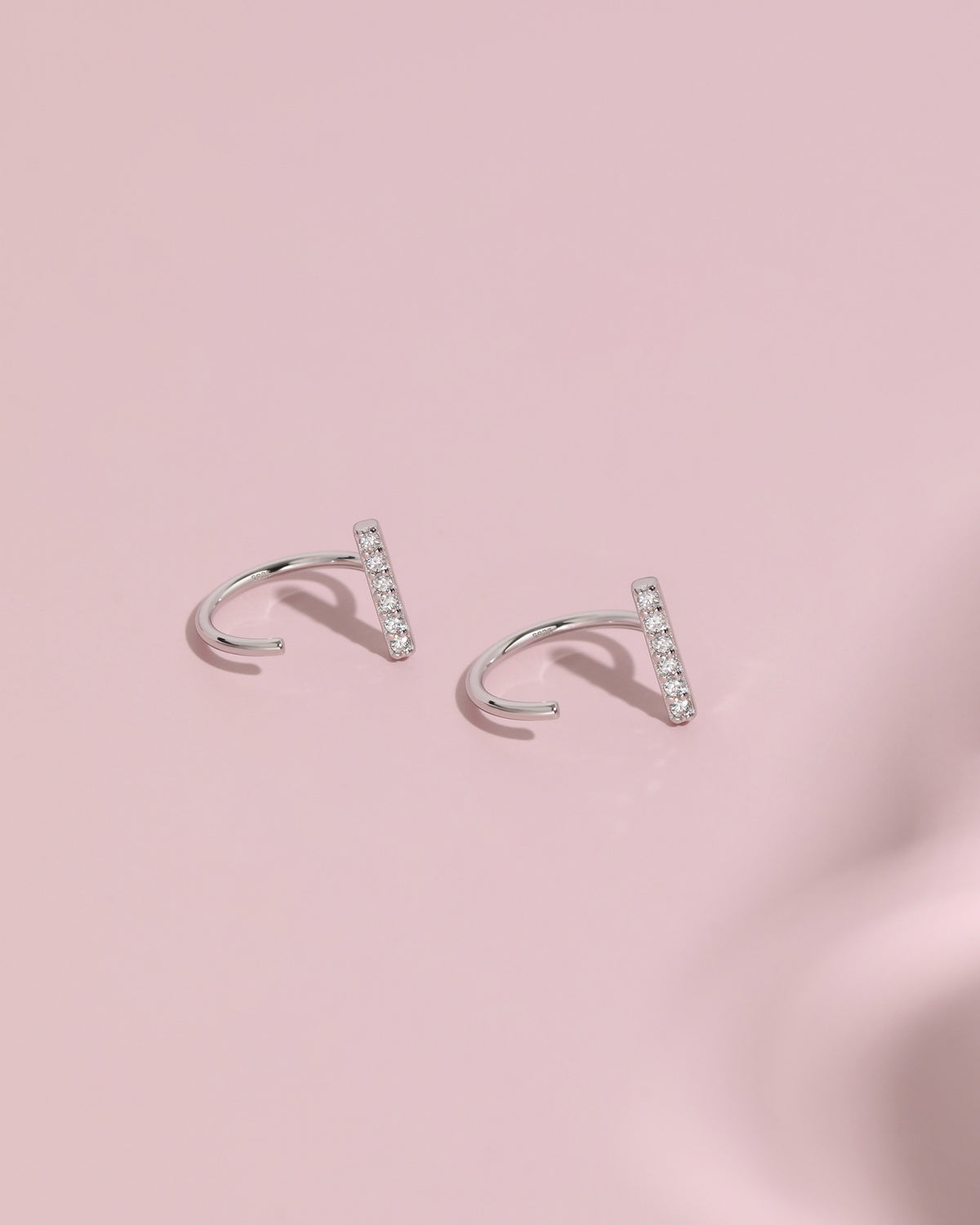 Pair of silver-tone Meissa Sparkling Bar Huggie Hoop Earrings with clear stones on a soft pink background.