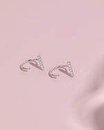 Pair of silver-tone Meissa Sparkling Bar Huggie Hoop Earrings with clear stones on a soft pink background.