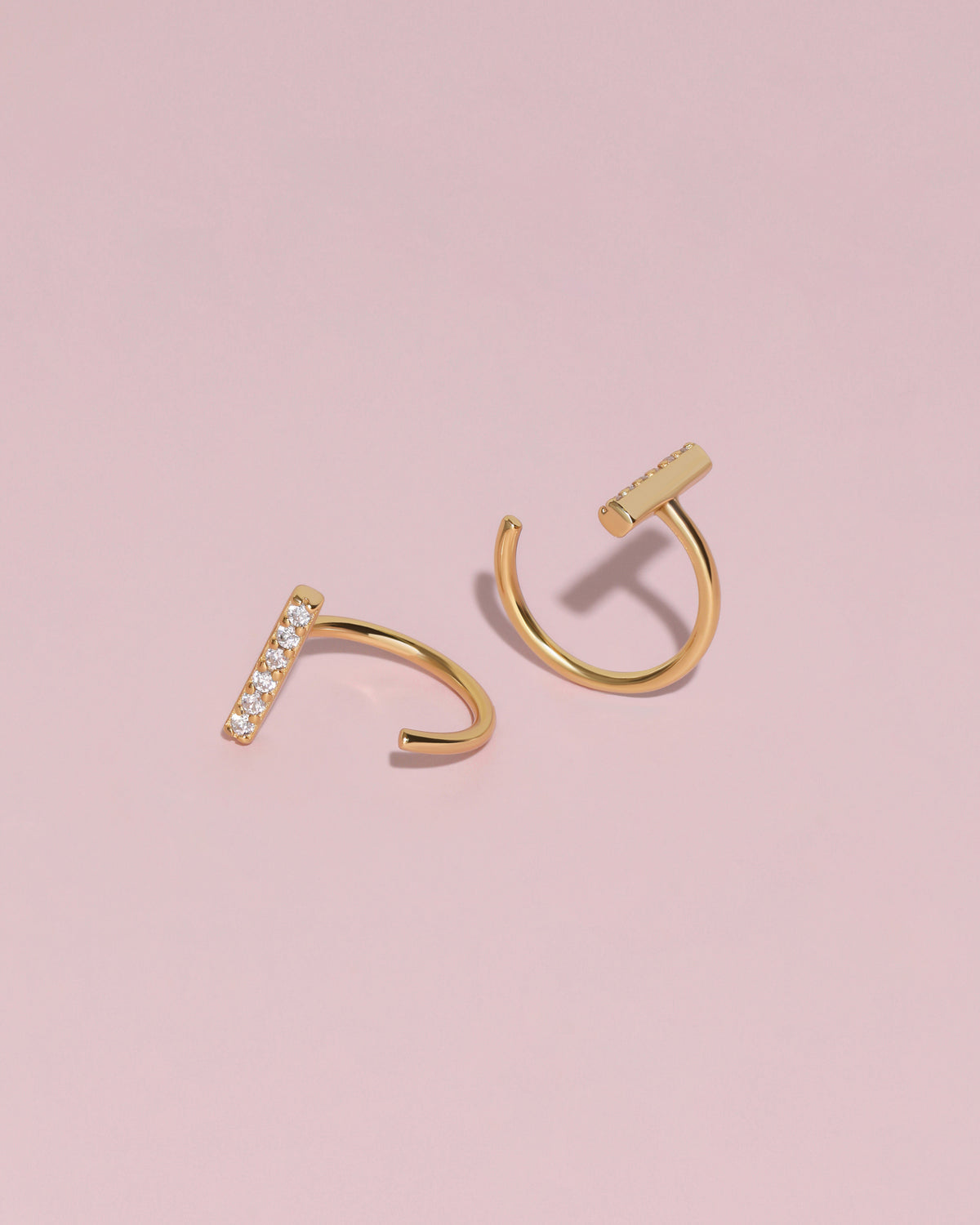 Gold-tone Meissa Sparkling Bar Huggie Hoop Earrings with clear stones shown from front and back angles on a soft pink background.