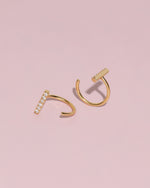 Pair of gold-tone Meissa Sparkling Bar Huggie Hoop Earrings with clear stones on a soft pink background.