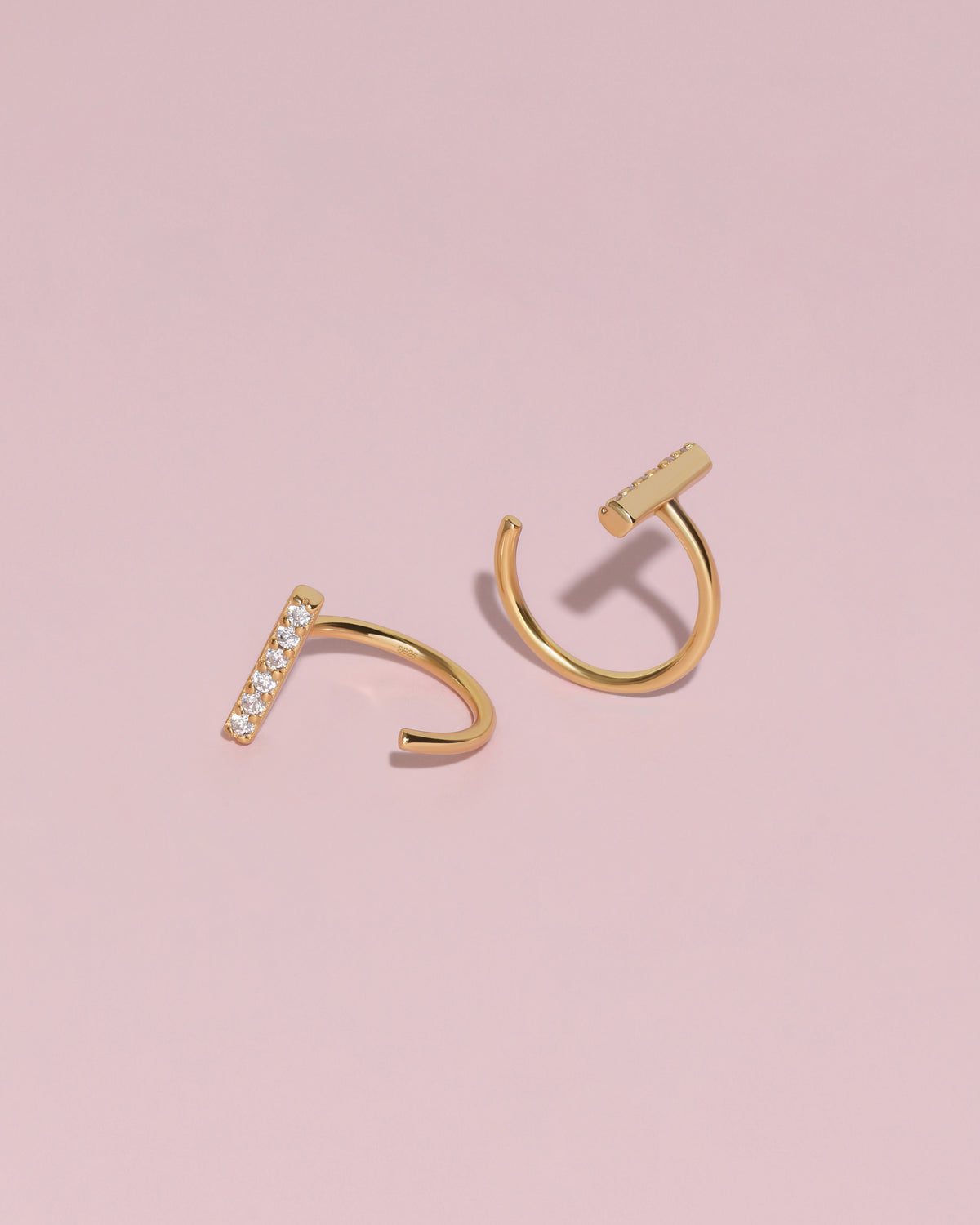Pair of gold-tone Meissa Sparkling Bar Huggie Hoop Earrings with clear stones on a soft pink background.