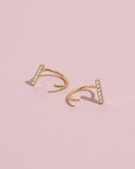 Pair of gold-tone Meissa Sparkling Bar Huggie Hoop Earrings with clear stones on a soft pink background.