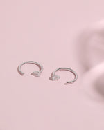 Pair of silver-tone Meissa Pear Sparkle Huggie Hoop Earrings with clear pear-cut stones on a soft pink background.