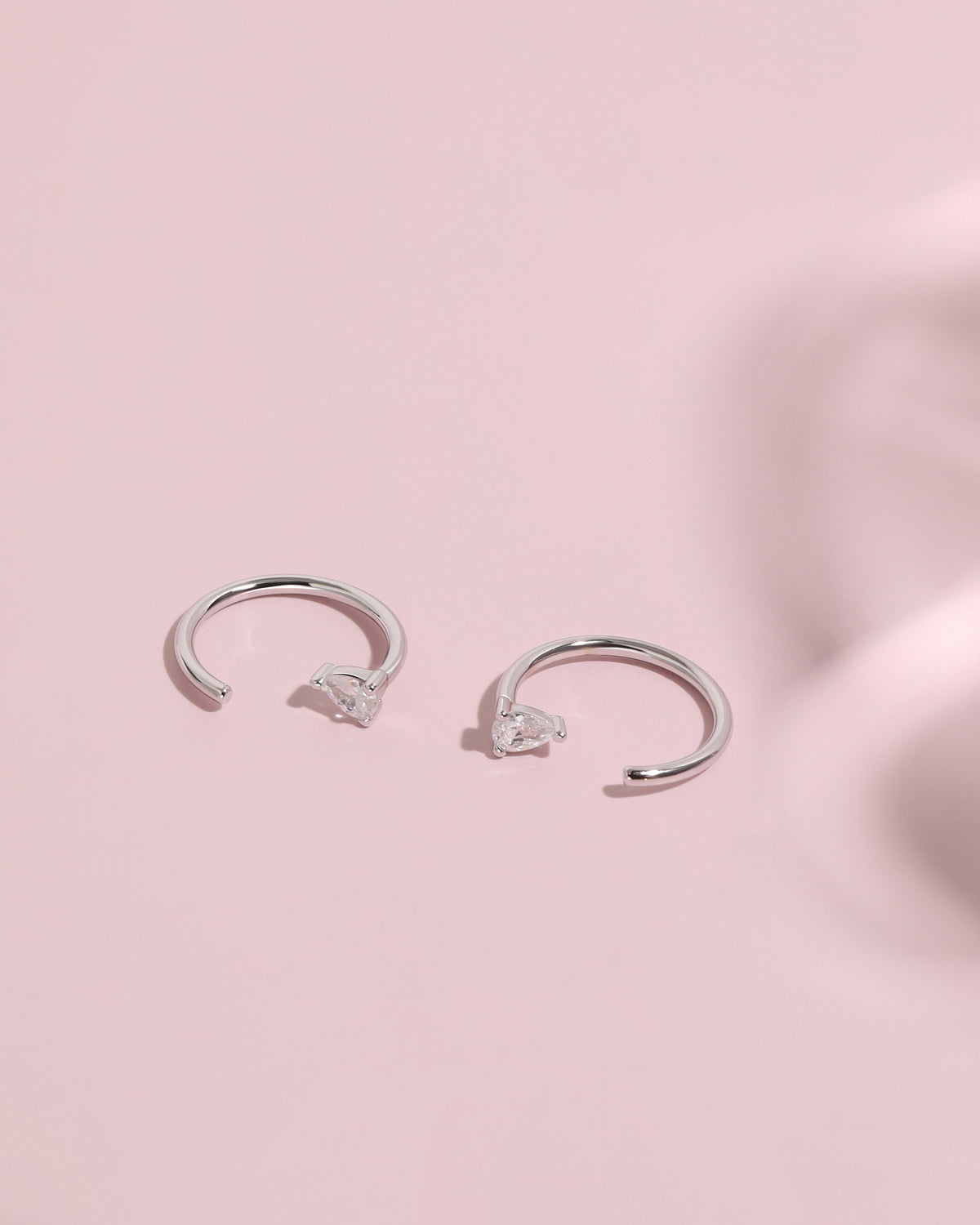 Pair of silver-tone Meissa Pear Sparkle Huggie Hoop Earrings with clear pear-cut stones on a soft pink background.