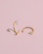 Pair of gold-tone Meissa Pear Sparkle Huggie Hoop Earrings with clear pear-cut stones on a soft pink background.