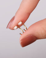 Close-up of gold-tone Meissa Baguette Sparkle Huggie Hoop Earrings with clear baguette-cut stones held between fingers.